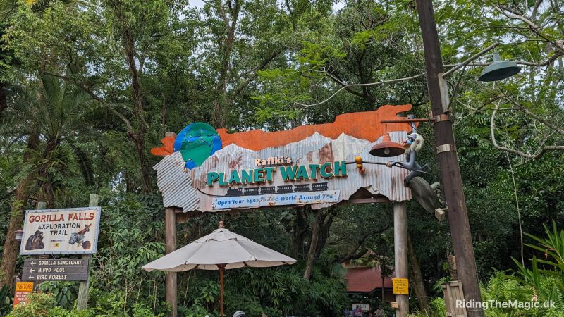 Rafiki's Planet Watch entrance sign at Animal Kingdom with a gorilla and umbrella in foreground