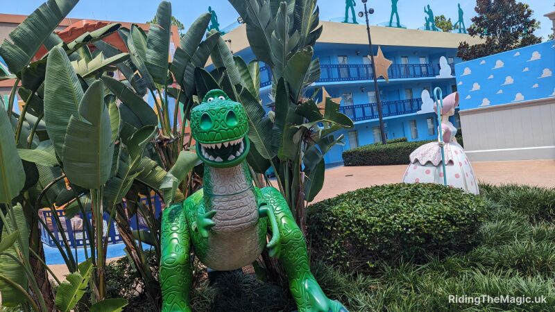 A photo of a green dinosaur statue in front of a blue building